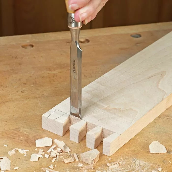 Hand using chisel to cut dovetail joints in wood on a workbench, woodworking tool detail