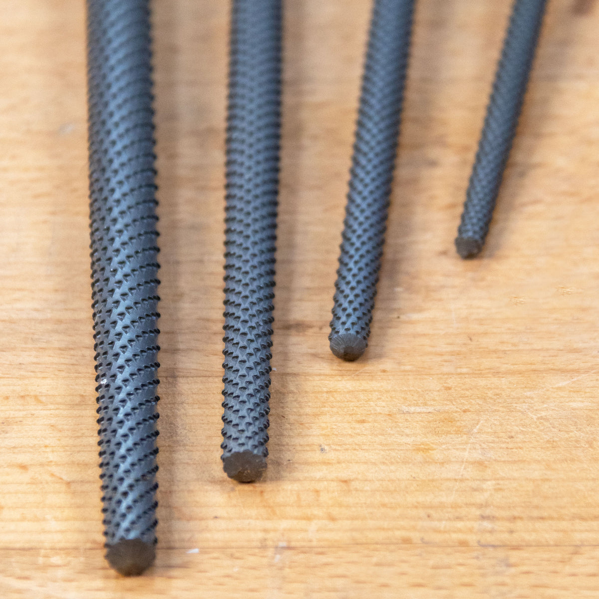 Closeup of the ends of 4 round rasps on a wooden work bench.