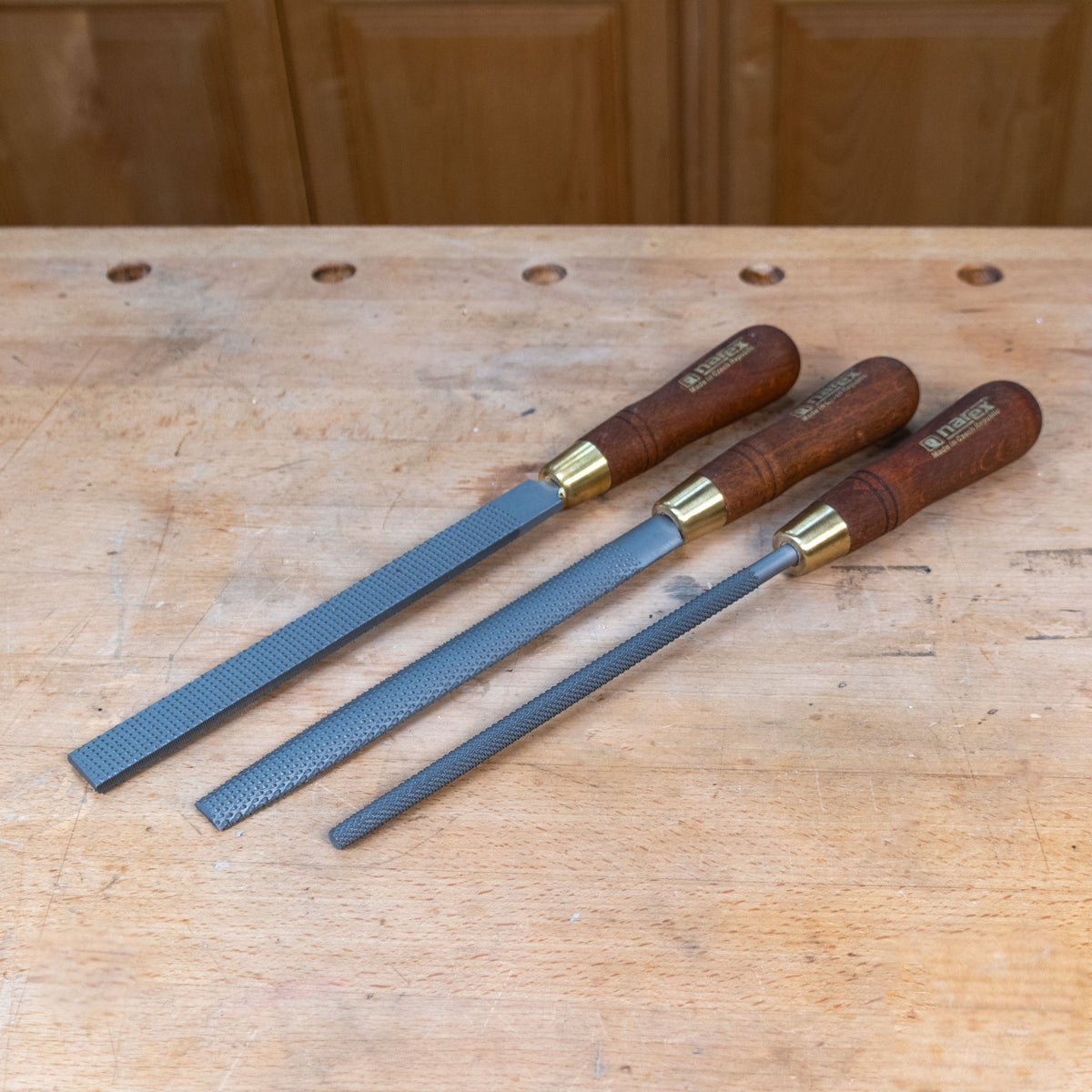 Three rasps, round, half round, and flat on a wooden work bench.