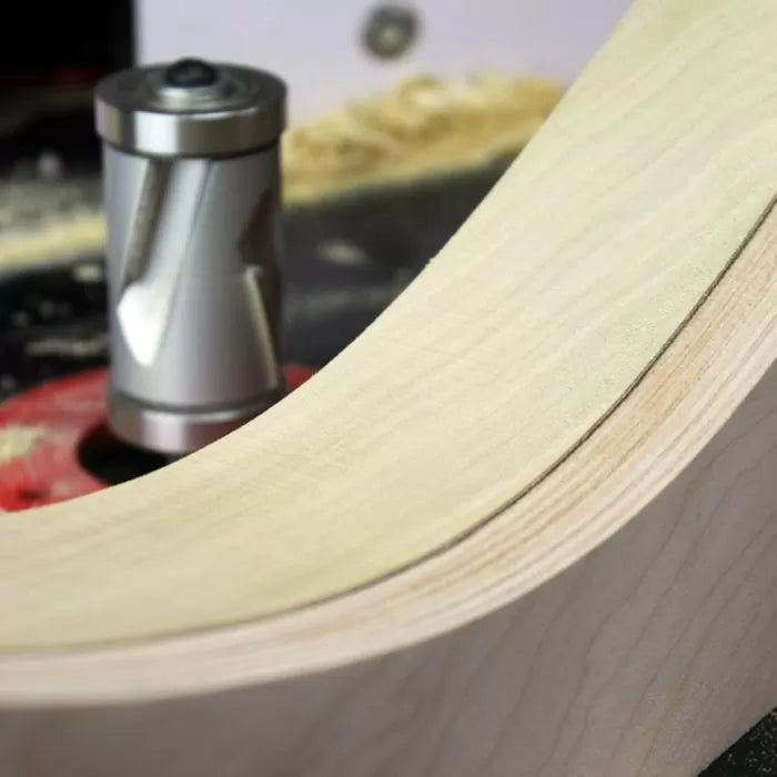 Spiral flush trim router bit shaping curved wood edge on a router table, with wood shavings visible.