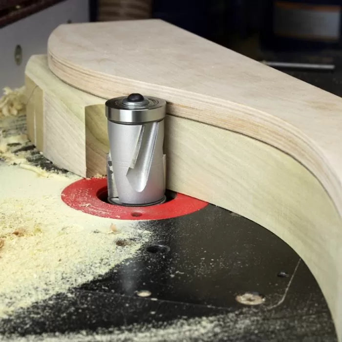 Template routing a curved wooden workpiece with a spiral router bit on a router table.