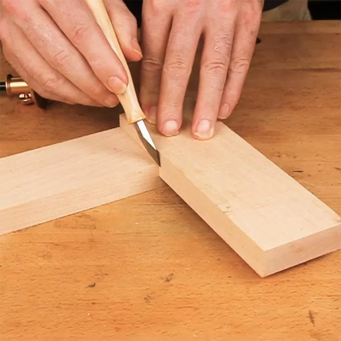 Hand using marking knife to scribe lines on woodworking project at a workbench