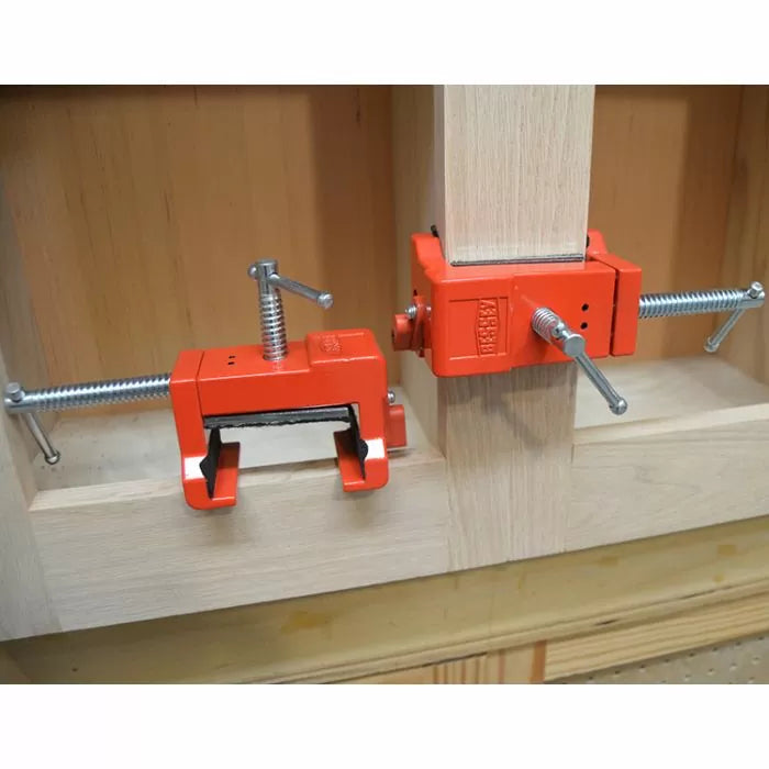 Red woodworking corner clamps securing wood panels for cabinet frame assembly