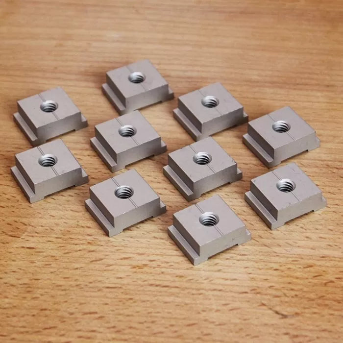 Set of ten square T-slot nuts for woodworking jigs on a wooden surface.
