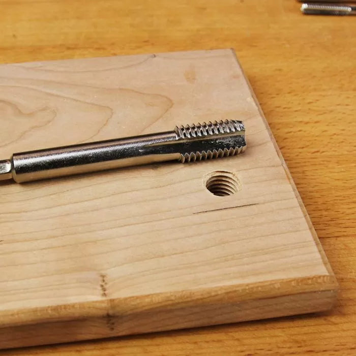 Steel threading tap tool on wooden board with threaded hole for woodworking projects