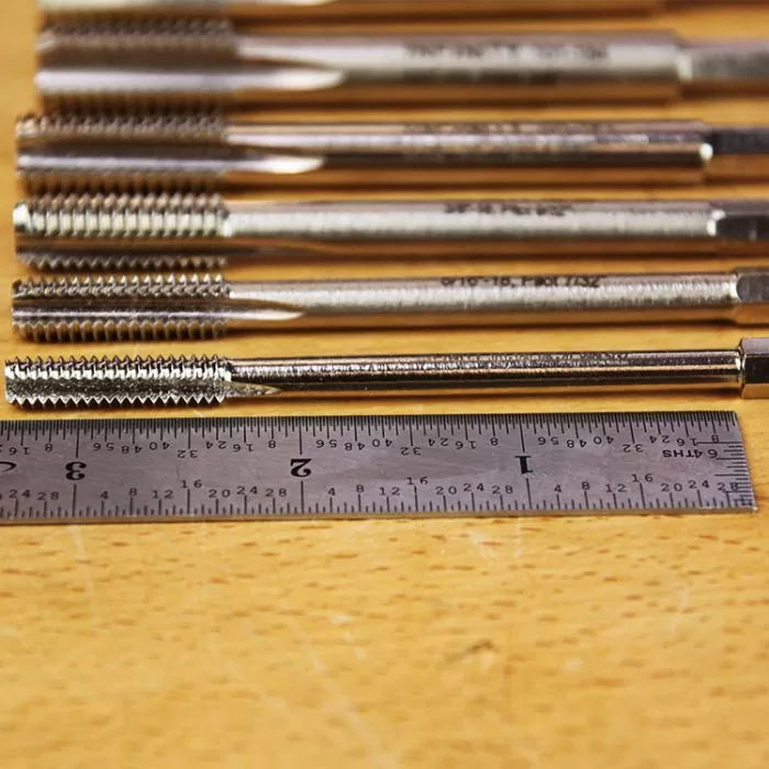 Metal thread taps aligned on workbench with steel ruler for woodworking tool measurement