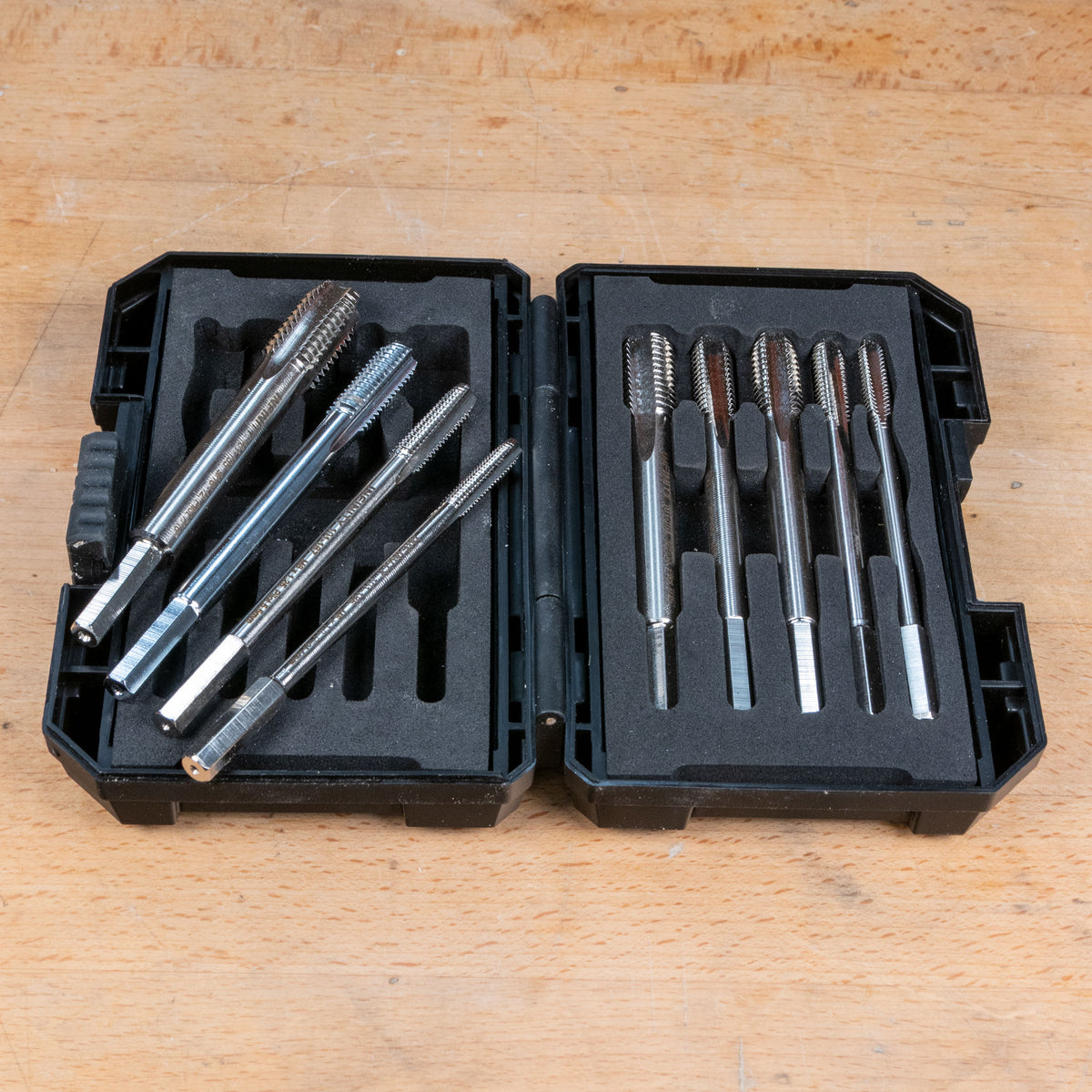 Metal tap and die set in black case on a wooden workbench, precision threading tools