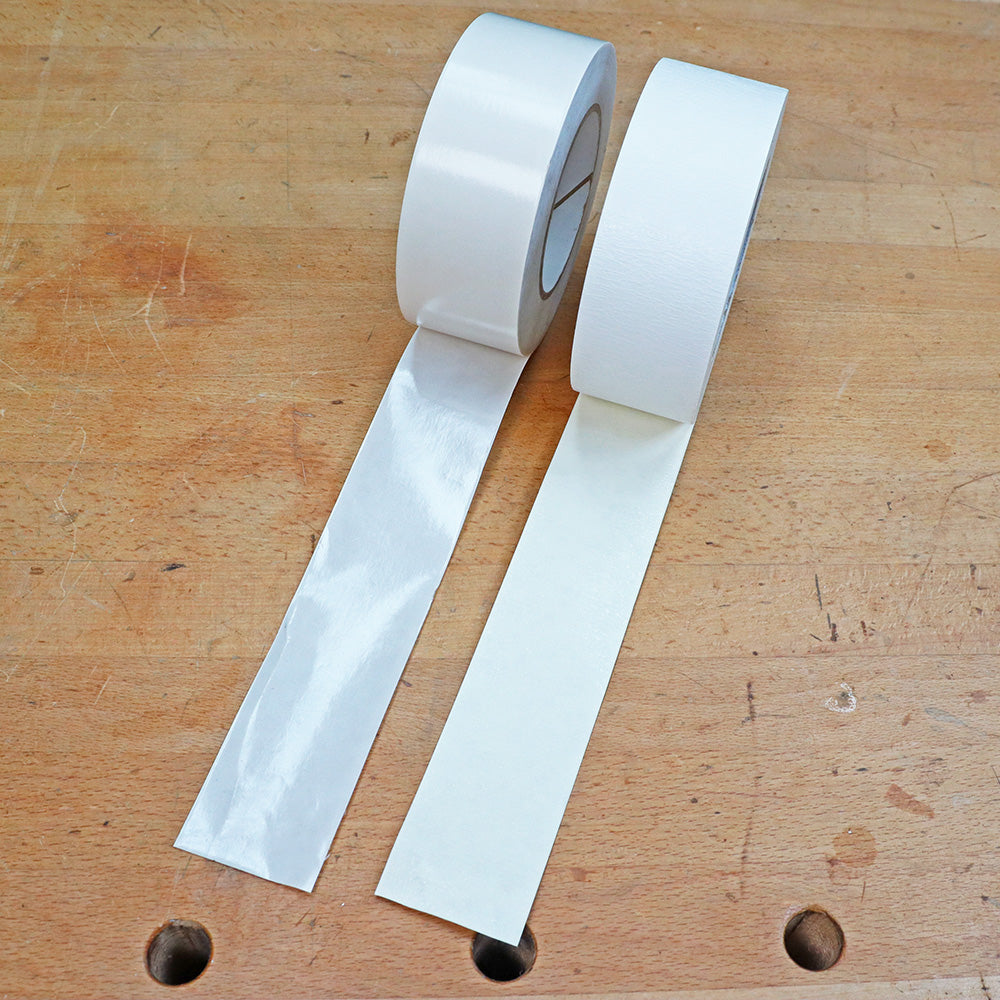 Two rolls of double-sided woodworking tape unspooled on a wood workbench.