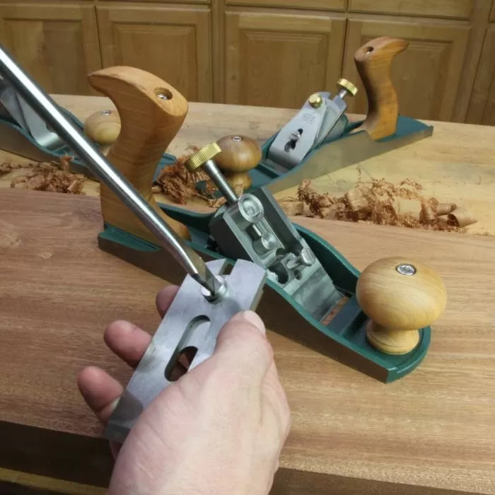 Hand adjusting woodworking hand plane on wooden workbench with shavings