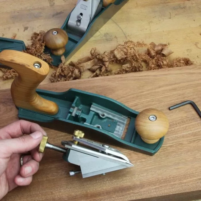 Hand removing frog mechanism from woodworking hand plane on workbench with wood shavings
