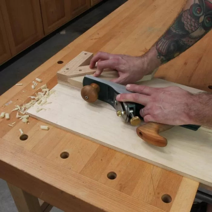 Woodworker using hand plane and shooting board on workbench for precise woodworking.