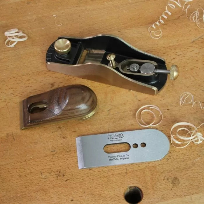 Disassembled hand plane with brass and wood parts on a workbench, woodworking tool