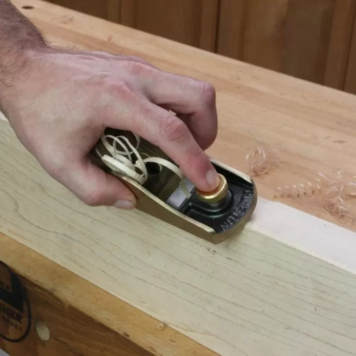 Hand using a block hand plane to smooth the edge of a wooden board on a workbench.