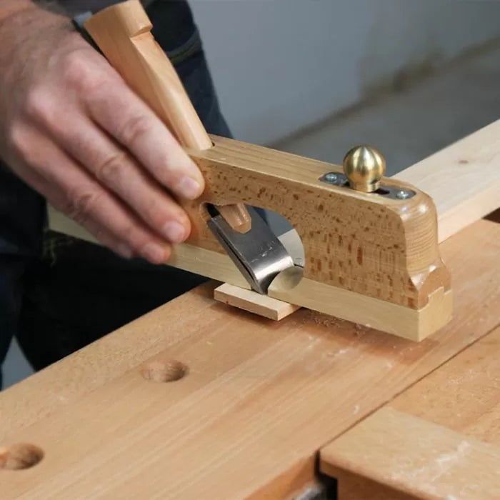 Woodworker using a wooden hand plane tool on a piece of wood at a workbench