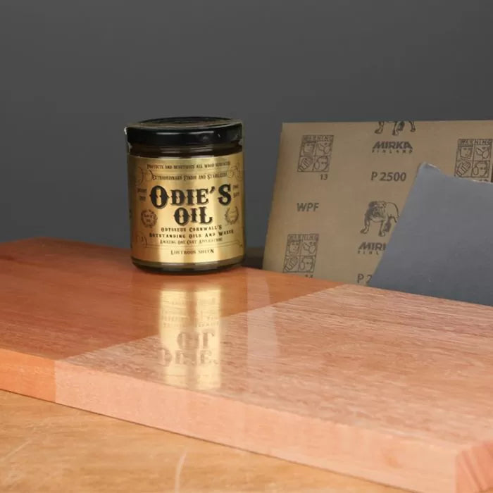 Odie's Oil wood finish jar on a polished wood board with sandpaper sheets