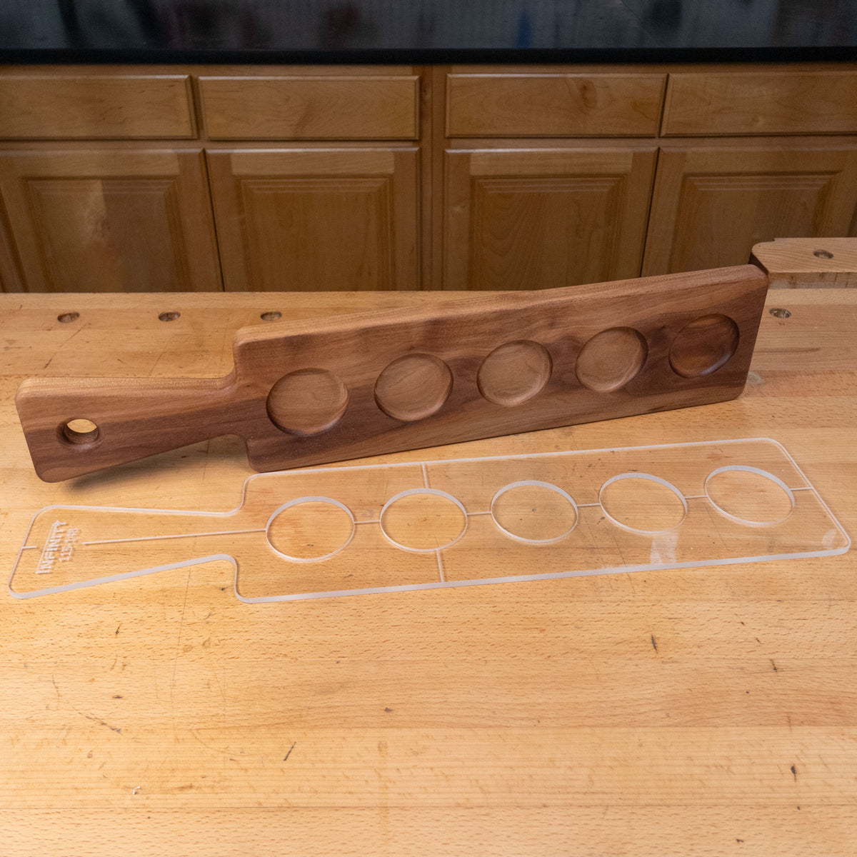 Acrylic cutting board template with four circular cutouts next to a matching wooden serving tray on a workbench.