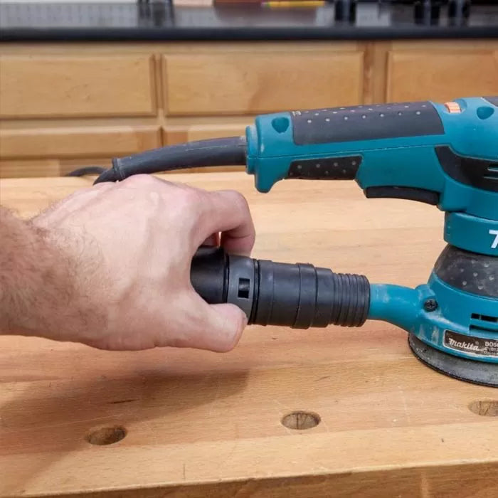 Hand attaching dust hose to orbital sander on woodworking bench, workshop background