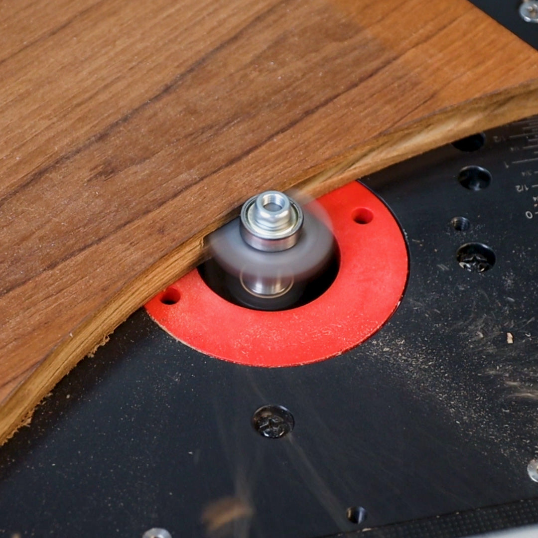 Wood board edge shaping on router table with spinning router bit and red insert ring