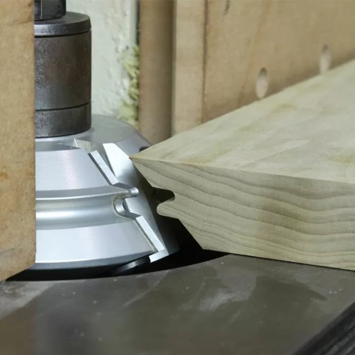 Wood shaper cutter head creating a tongue and groove joint on a wooden board