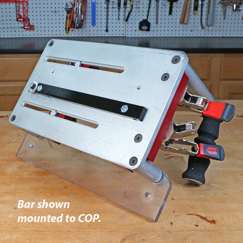 Woodworking clamping fixture with metal bar and red handles mounted on workbench.