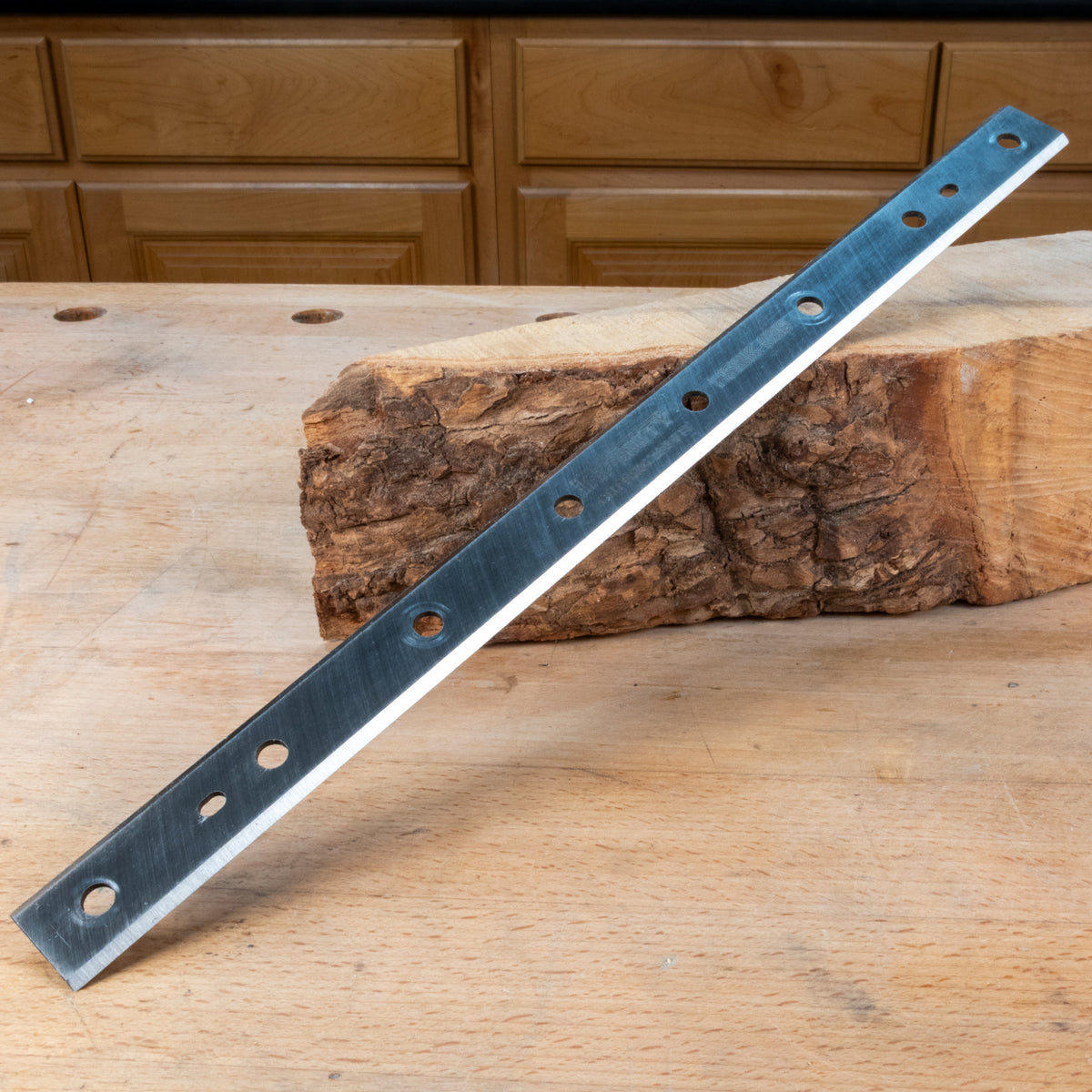 Long metal jointer knife blade with holes on a wooden surface