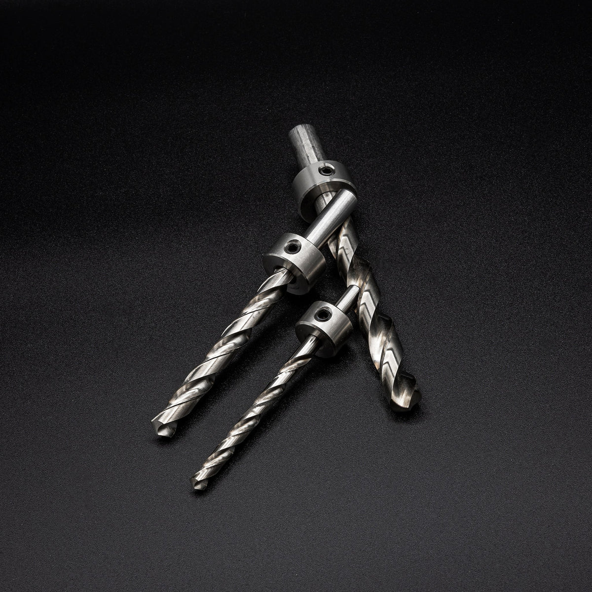 Three metal drill bits with stop collars on a black background, woodworking tool closeup