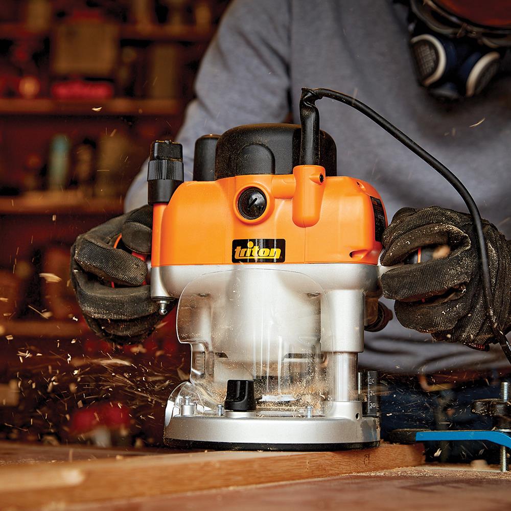 Woodworker using an electric plunge router on wood, producing sawdust in workshop
