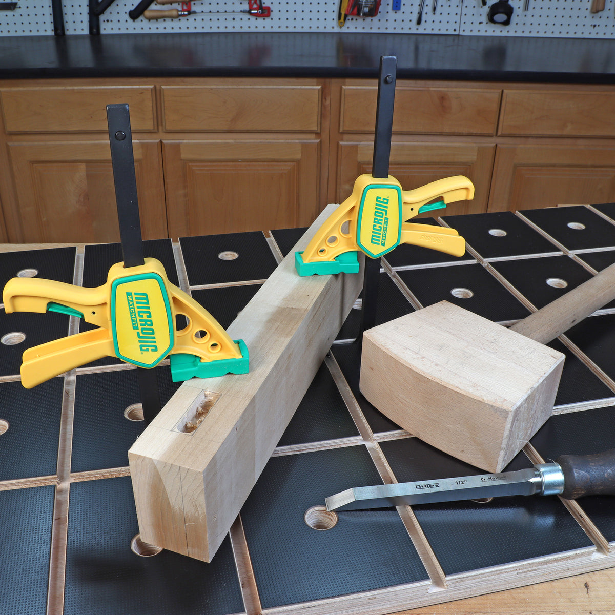 Woodworking clamps securing lumber on a workbench with mallet and chisel nearby