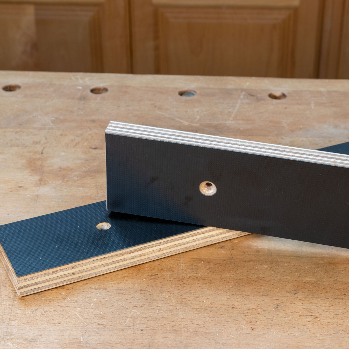 Close-up of two MDF phenolic bench dog plates with mounting holes on a woodworking table.