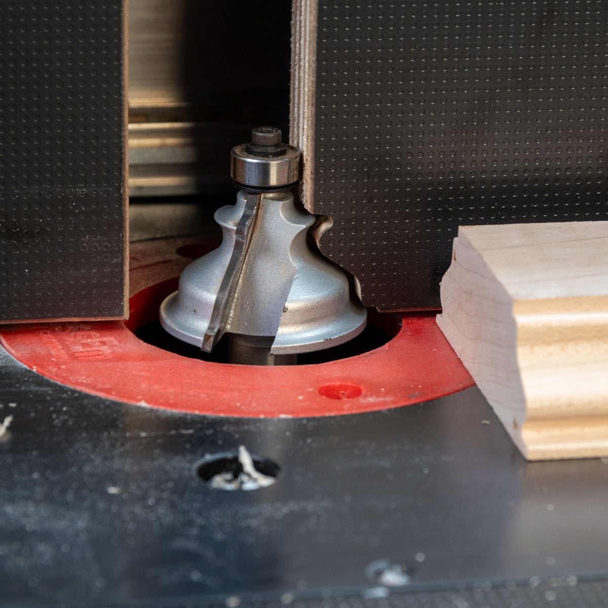 Close-up of a router table with roundover router bit cutting molding profile on wood piece