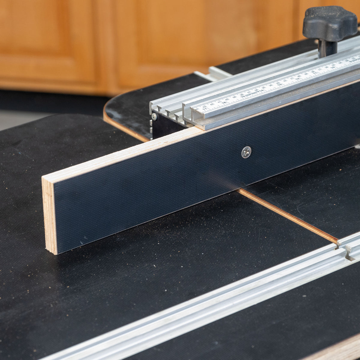 Closeup of a router table extension with MDF fence, ruler, and adjustment knob for woodworking.
