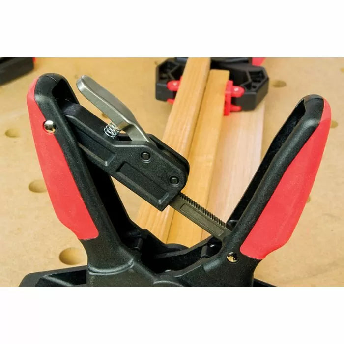 Close-up of quick-release woodworking clamp holding wooden boards on a workbench