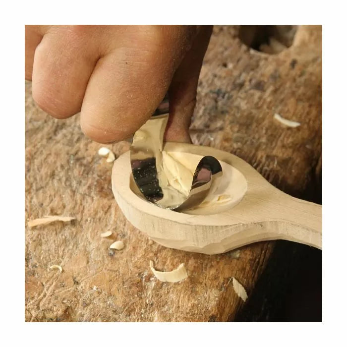 Hand using a curved wood carving tool to shape a wooden spoon on a workbench