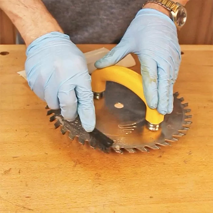 Person cleaning circular saw blade with safety handle and brush on workbench