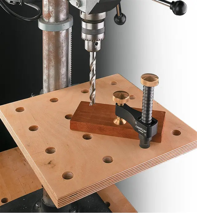 Drill press with woodworking clamp holding a board on a perforated workbench