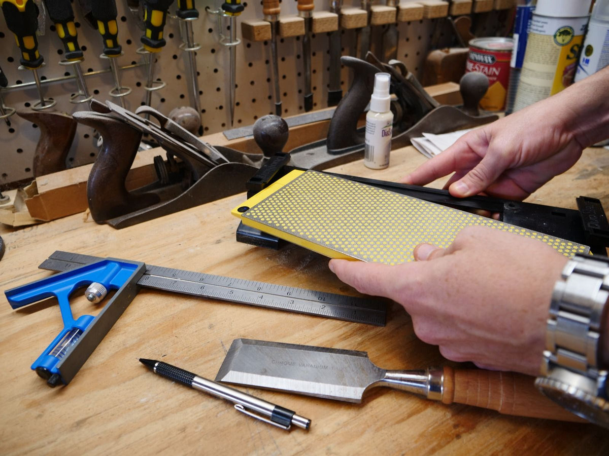 Woodworker sharpening chisel with diamond sharpening stone on a workbench, surrounded by hand tools