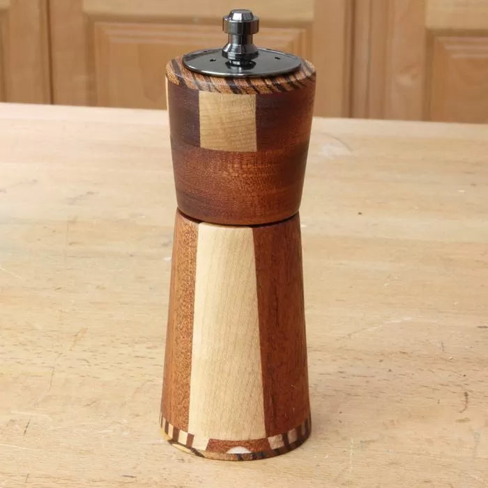 Handcrafted wooden pepper mill on a woodworking table, featuring contrasting wood tones.
