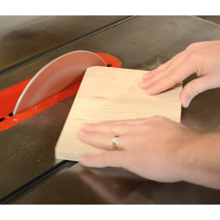Hands guiding a wooden board through a table saw for precise woodworking cut