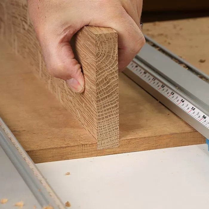 Hand holding a wooden board on a router table with a measuring guide, woodworking setup