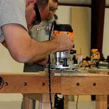 Woodworker guiding a router along a workbench in a hands-on woodworking class