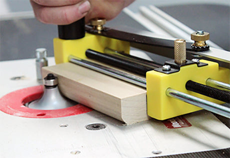 Yellow featherboard hold-down guiding a board past a bearing router bit on a router table