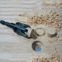 Plug cutter beside a wood plug and drilled hole on a board with shavings