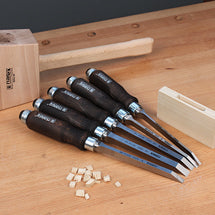 Set of bench chisels with dark handles laid out beside a wooden mallet