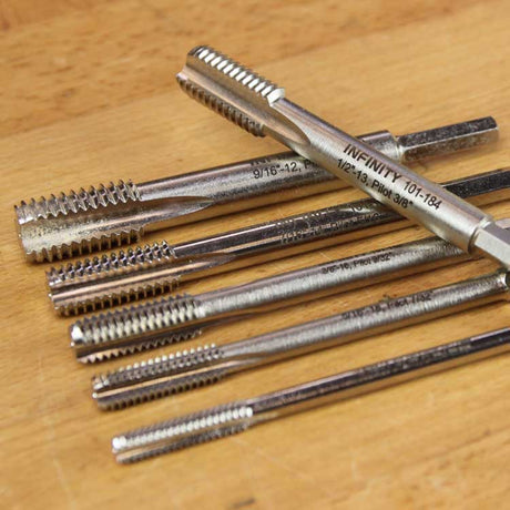 Infinity wood taps in assorted thread sizes laid out on a wood surface