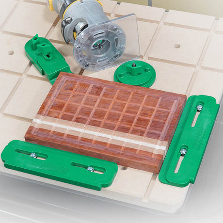 Green CNC hold-down clamps securing a striped end-grain cutting board beside a router