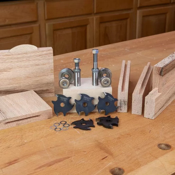 Woodworking slot cutter router bits with bearings, blades, and sample joints on a workbench