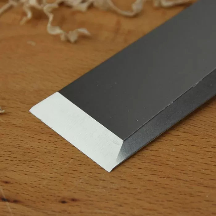 Close-up of a sharp woodworking chisel blade on a wooden surface with wood shavings