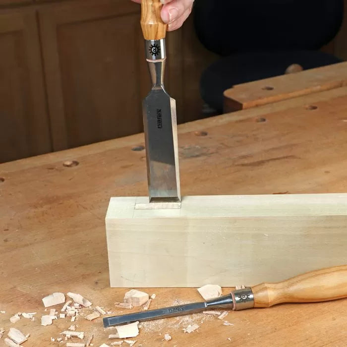 Wood chisel carving mortise joint in block of wood on woodworking bench
