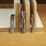Carbide spiral router bits displayed upright in front of stacked plywood sheets on a workbench