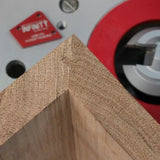 Close-up of a precise woodworking miter joint on a wooden frame next to a router table.